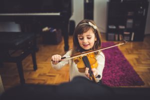 Young cute girl playing violin at home
